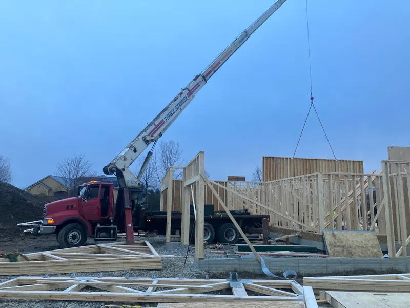 A ROC Crane boom truck setting a framed wall panel onto a house foundation at first light.